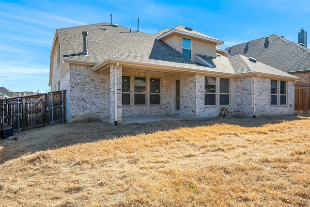 rear view of house featuring brick siding, a shingled roof, fence, a yard, and a patio