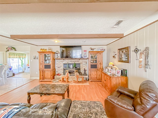 living area with visible vents, beamed ceiling, light wood-type flooring, a wood stove, and a textured ceiling