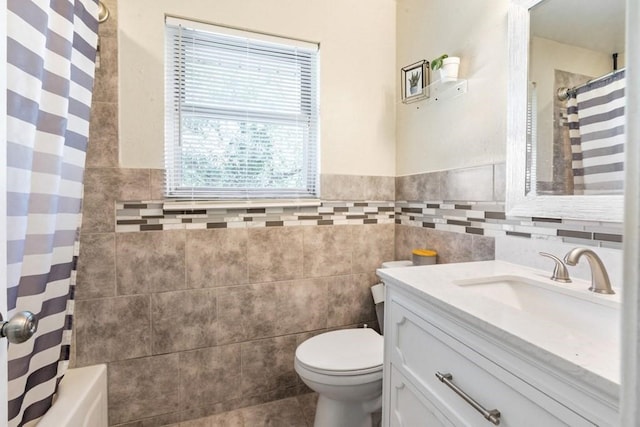 bathroom featuring a wainscoted wall, toilet, vanity, tile patterned flooring, and tile walls