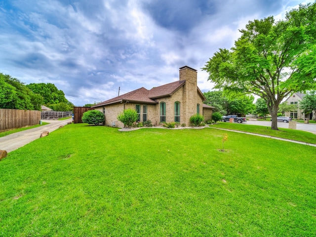 view of front of house featuring fence, a chimney, a front lawn, concrete driveway, and brick siding