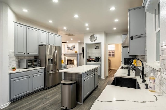 kitchen featuring gray cabinetry, stainless steel refrigerator with ice dispenser, a sink, a center island, and recessed lighting