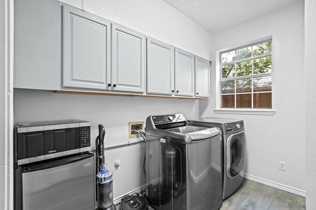 clothes washing area featuring washer and clothes dryer, cabinet space, light wood finished floors, and baseboards