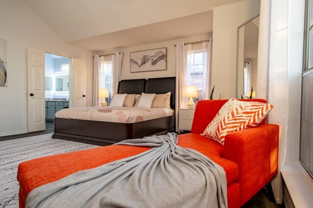 bedroom featuring ensuite bath, vaulted ceiling, multiple windows, and baseboards