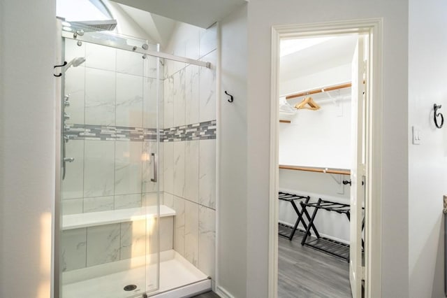 full bath with a stall shower, a walk in closet, and wood finished floors