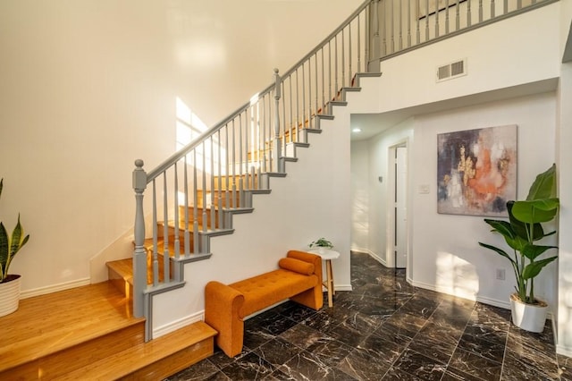 stairs with visible vents, marble finish floor, a high ceiling, and baseboards