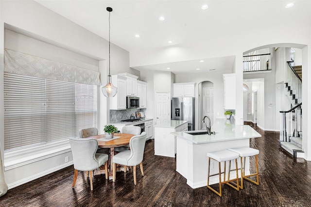 kitchen with a kitchen island, arched walkways, a sink, stainless steel appliances, and tasteful backsplash