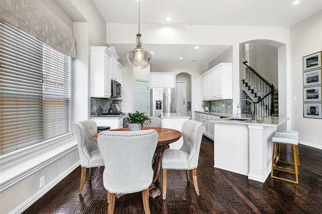 dining area with arched walkways, stairway, dark wood finished floors, and baseboards