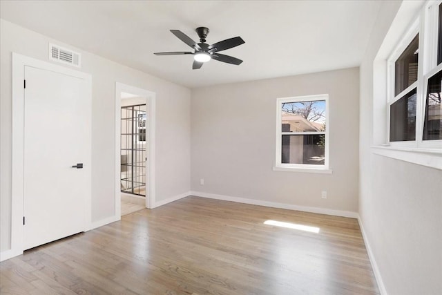 empty room featuring a ceiling fan, wood finished floors, visible vents, and baseboards