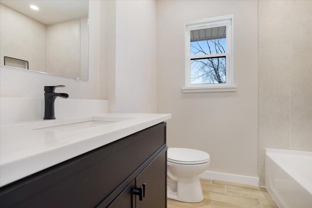 full bath with wood finish floors, baseboards, toilet, a bathing tub, and vanity