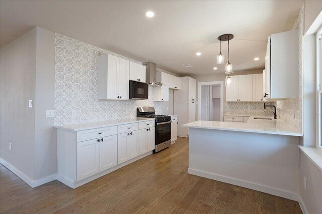 kitchen featuring a peninsula, a sink, black microwave, wall chimney exhaust hood, and stainless steel gas stove