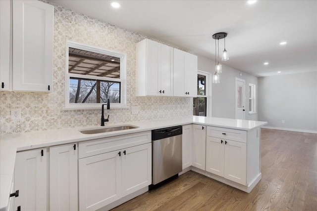 kitchen with dishwasher, a peninsula, white cabinetry, and a sink