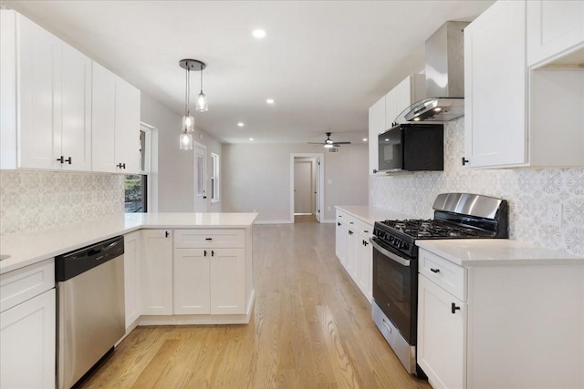 kitchen with gas stove, a peninsula, black microwave, dishwasher, and wall chimney range hood