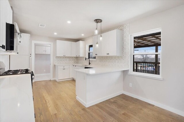 kitchen with light countertops, decorative backsplash, a peninsula, light wood-style floors, and white cabinets