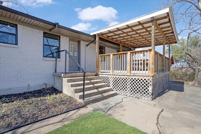 view of exterior entry with brick siding, a deck, and a carport