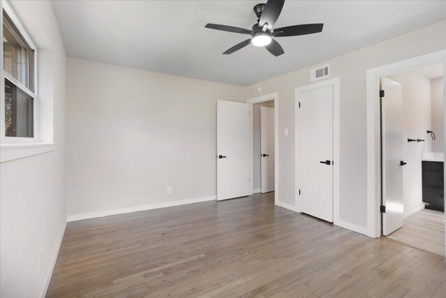 unfurnished bedroom featuring visible vents, baseboards, light wood-type flooring, ensuite bath, and a ceiling fan