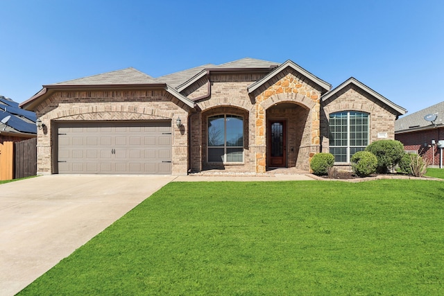 french provincial home with a front lawn, concrete driveway, a shingled roof, a garage, and brick siding