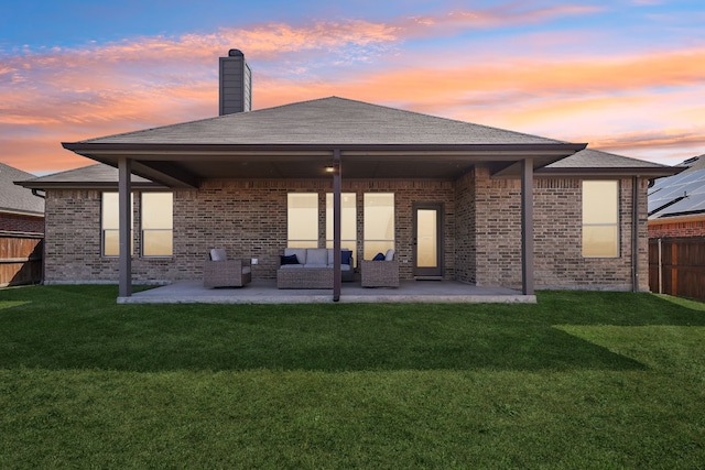 back of house at dusk with a yard, outdoor lounge area, a patio, and fence