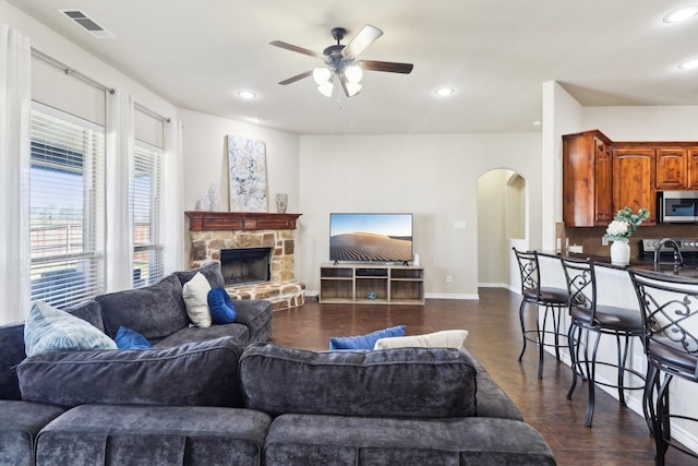 living area featuring visible vents, dark wood-style floors, arched walkways, a fireplace, and ceiling fan