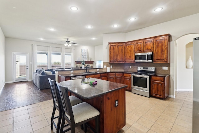 kitchen with light tile patterned floors, a peninsula, arched walkways, a sink, and appliances with stainless steel finishes