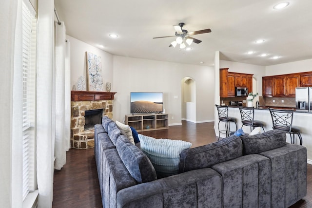 living area featuring ceiling fan, dark wood-style floors, recessed lighting, a stone fireplace, and arched walkways