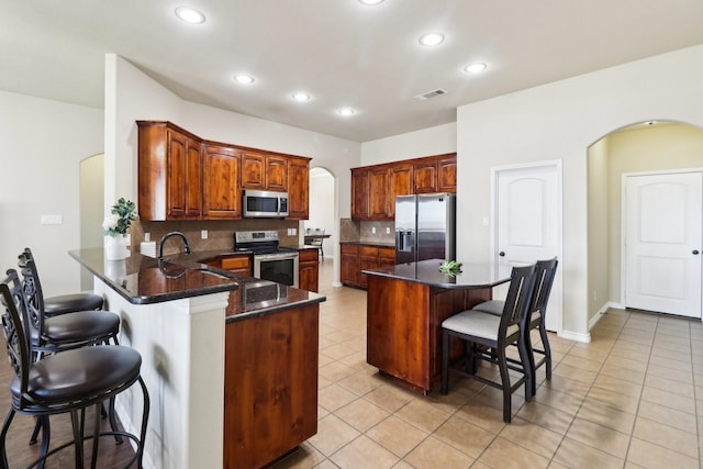 kitchen with visible vents, arched walkways, a sink, stainless steel appliances, and a kitchen breakfast bar