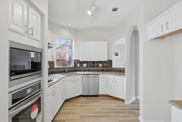 kitchen featuring light wood-type flooring, decorative backsplash, stainless steel appliances, white cabinetry, and a sink