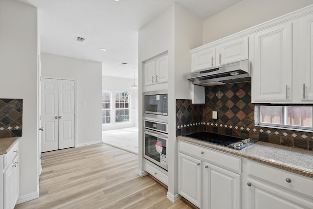 kitchen with white cabinets, light wood-style floors, under cabinet range hood, appliances with stainless steel finishes, and tasteful backsplash