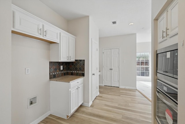 kitchen with light wood finished floors, backsplash, baseboards, stainless steel appliances, and white cabinetry