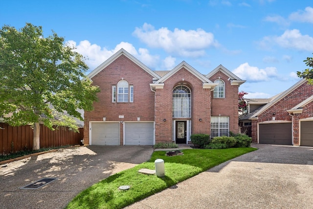 traditional home featuring brick siding, driveway, an attached garage, and fence