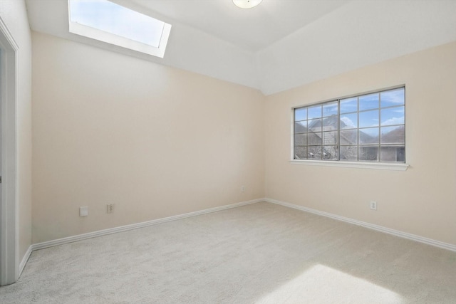 empty room featuring carpet flooring, vaulted ceiling with skylight, and baseboards