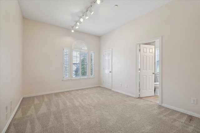 unfurnished room with rail lighting, baseboards, and carpet