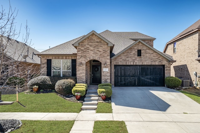 french provincial home with driveway, an attached garage, a shingled roof, a front lawn, and brick siding