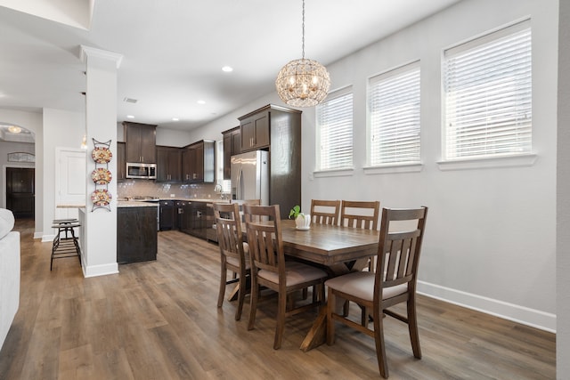 dining space with a notable chandelier, recessed lighting, arched walkways, light wood-style floors, and baseboards