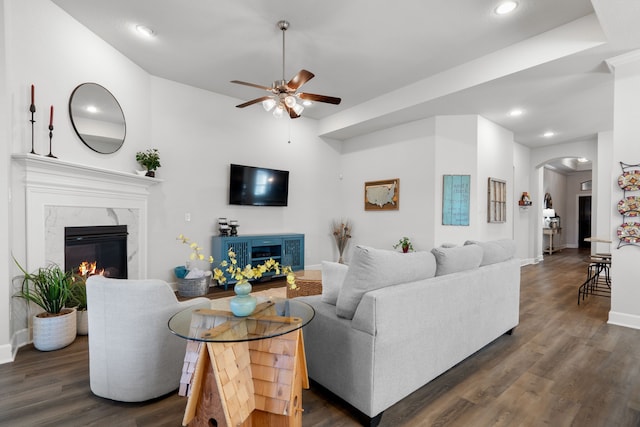 living room with arched walkways, a fireplace, dark wood-type flooring, and ceiling fan