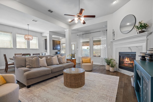 living area featuring visible vents, a premium fireplace, dark wood-style flooring, and decorative columns