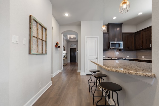 kitchen with tasteful backsplash, stainless steel microwave, light stone countertops, a breakfast bar, and arched walkways