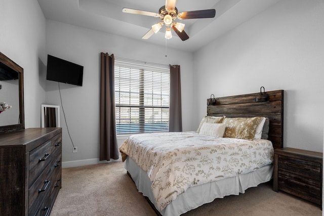 bedroom with light carpet, ceiling fan, a tray ceiling, and baseboards