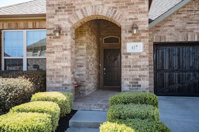 view of exterior entry with brick siding and roof with shingles