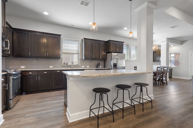 kitchen with visible vents, a breakfast bar, tasteful backsplash, stainless steel appliances, and dark brown cabinetry