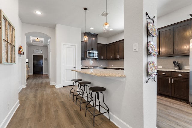 kitchen with light wood-type flooring, visible vents, stainless steel microwave, a kitchen breakfast bar, and dark brown cabinetry