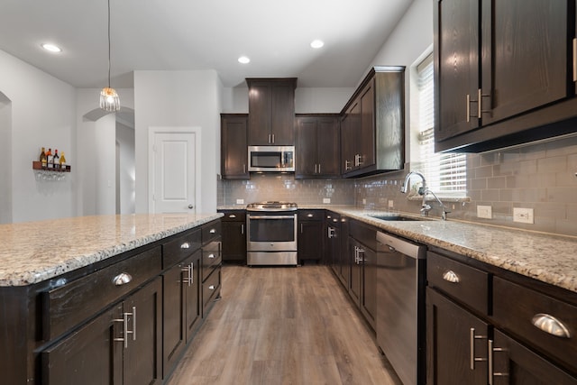 kitchen with a sink, backsplash, stainless steel appliances, dark brown cabinetry, and light wood finished floors