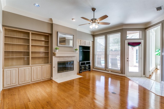 unfurnished living room with visible vents, ornamental molding, a tiled fireplace, light wood finished floors, and ceiling fan