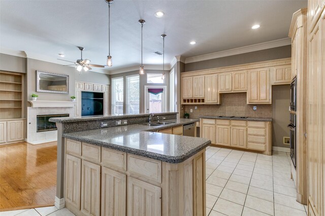 kitchen featuring light brown cabinetry, ornamental molding, appliances with stainless steel finishes, a glass covered fireplace, and a sink