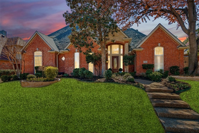 view of front of property with brick siding, a yard, and roof with shingles