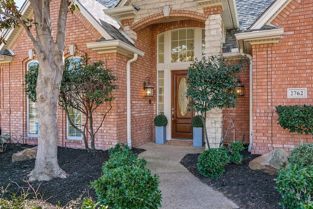 property entrance featuring brick siding and roof with shingles