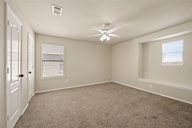 carpeted empty room featuring a ceiling fan, visible vents, and baseboards