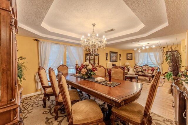 dining area featuring visible vents, a tray ceiling, light wood-style flooring, a notable chandelier, and a textured ceiling