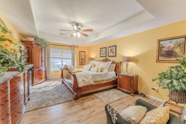 bedroom with visible vents, a textured ceiling, light wood-type flooring, and a tray ceiling