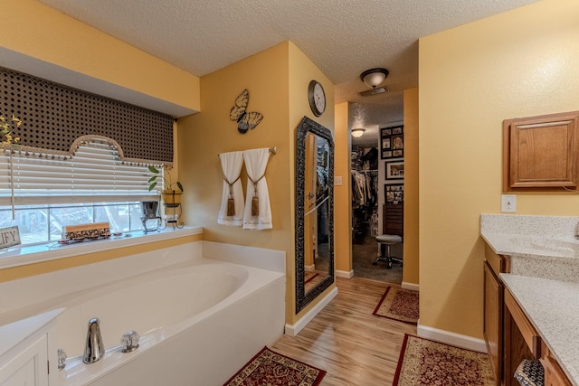 bathroom featuring a textured ceiling, vanity, a garden tub, and wood finished floors