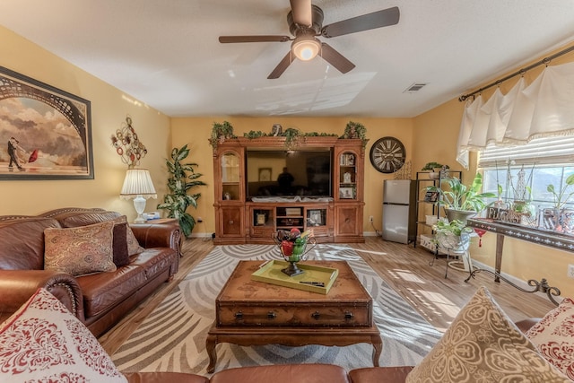 living room featuring baseboards, visible vents, light wood finished floors, and ceiling fan